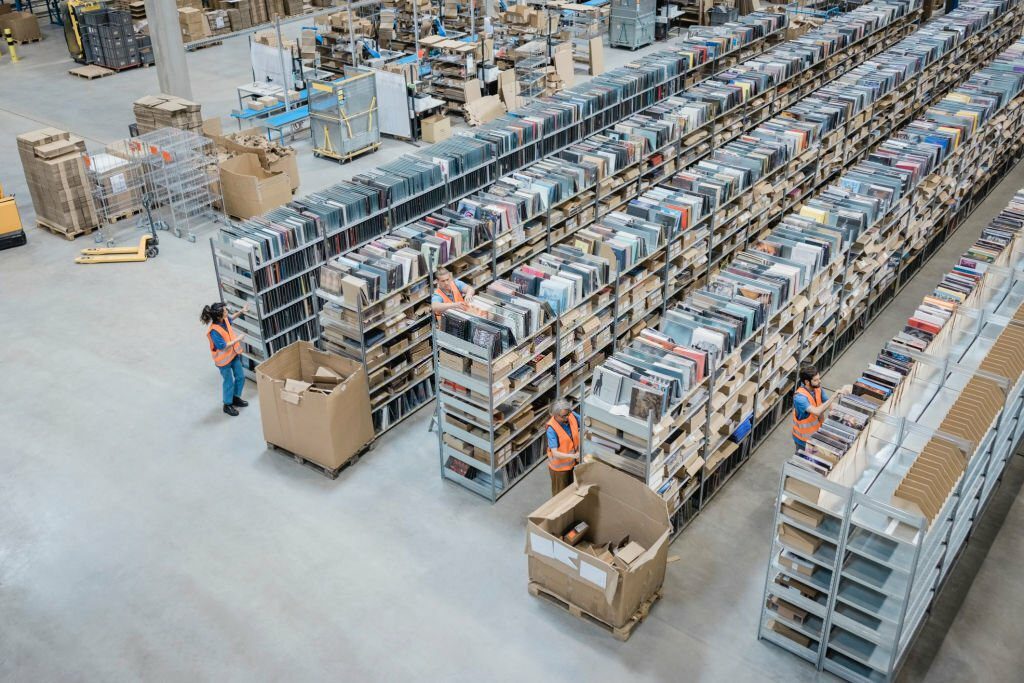 High angle view of a large shipping company warehouse with people working. Large shelves and racks in distribution warehouse with public records management of employees working